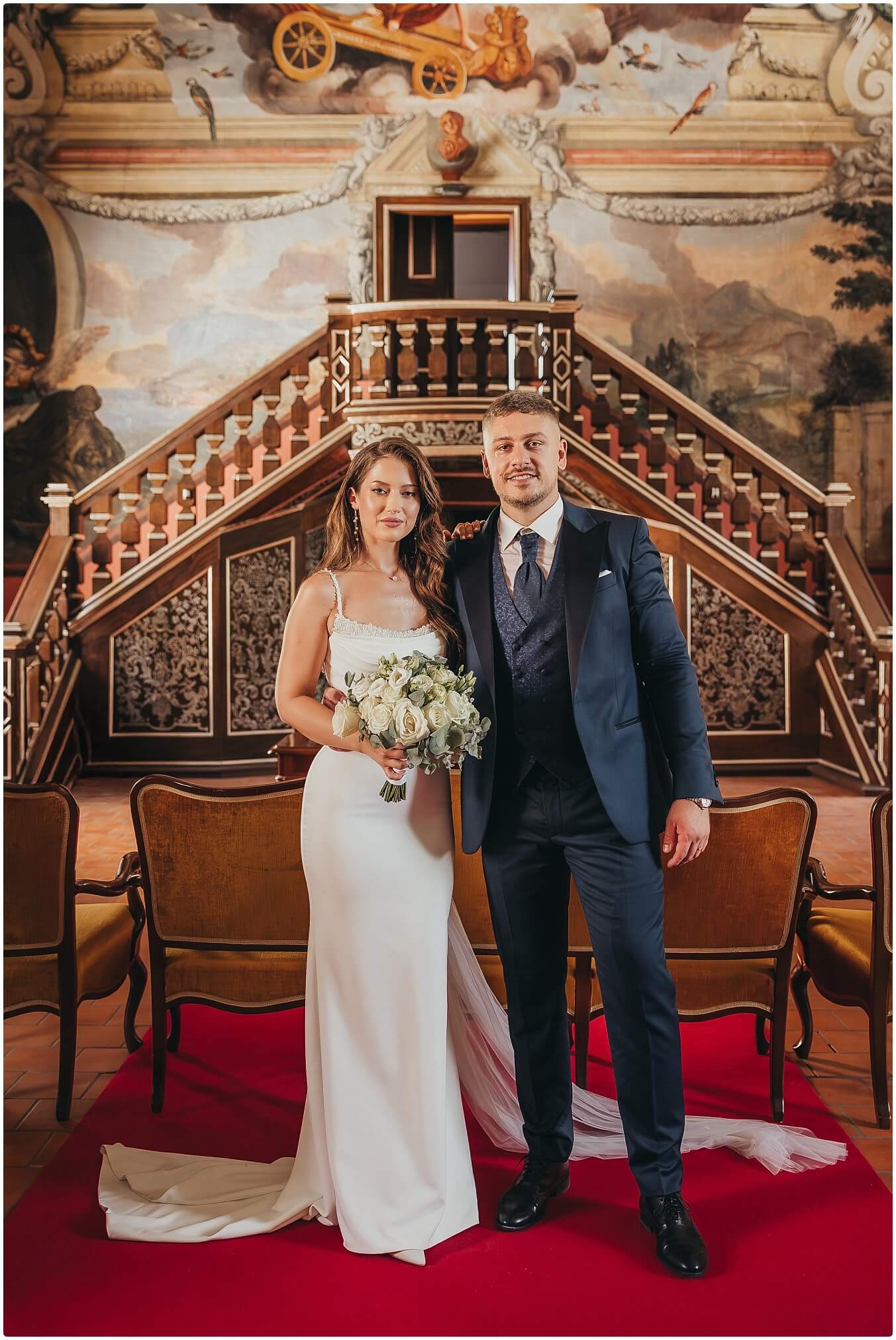 Vjenčani par zagrljen na stepenicama dvorca u elegantnoj atmosferi