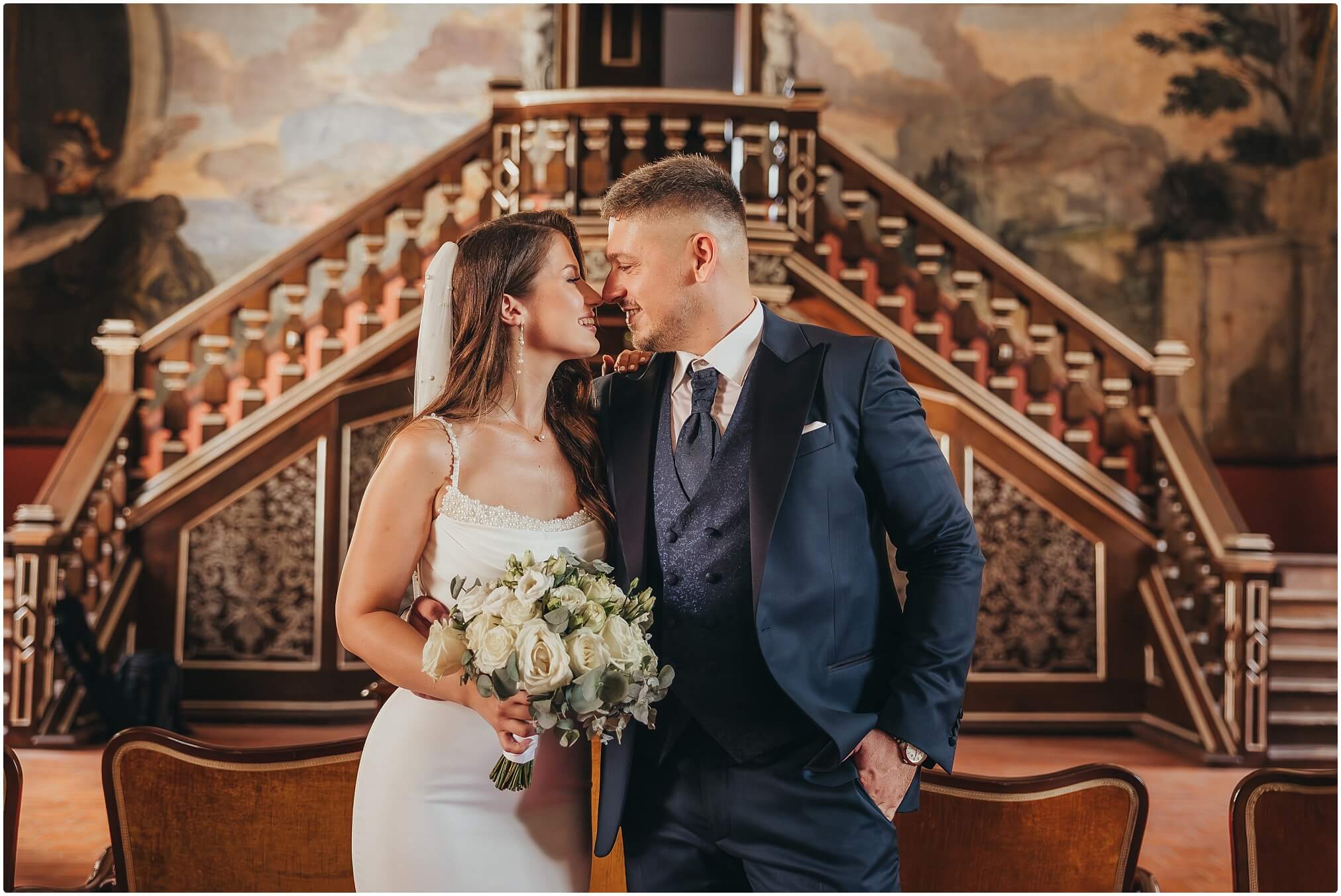 Vjenčani par zagrljen na stepenicama dvorca u elegantnoj atmosferi