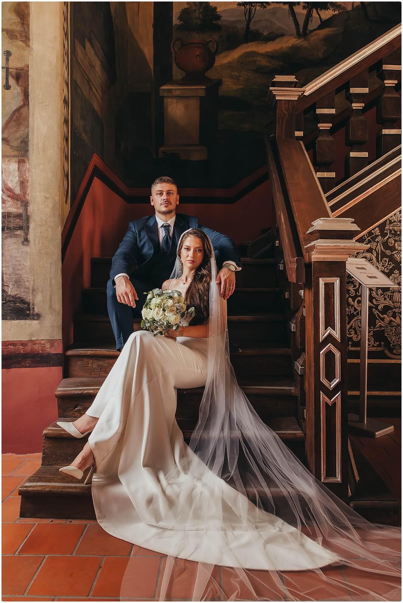 Vjenčani par zagrljen na stepenicama dvorca u elegantnoj atmosferi