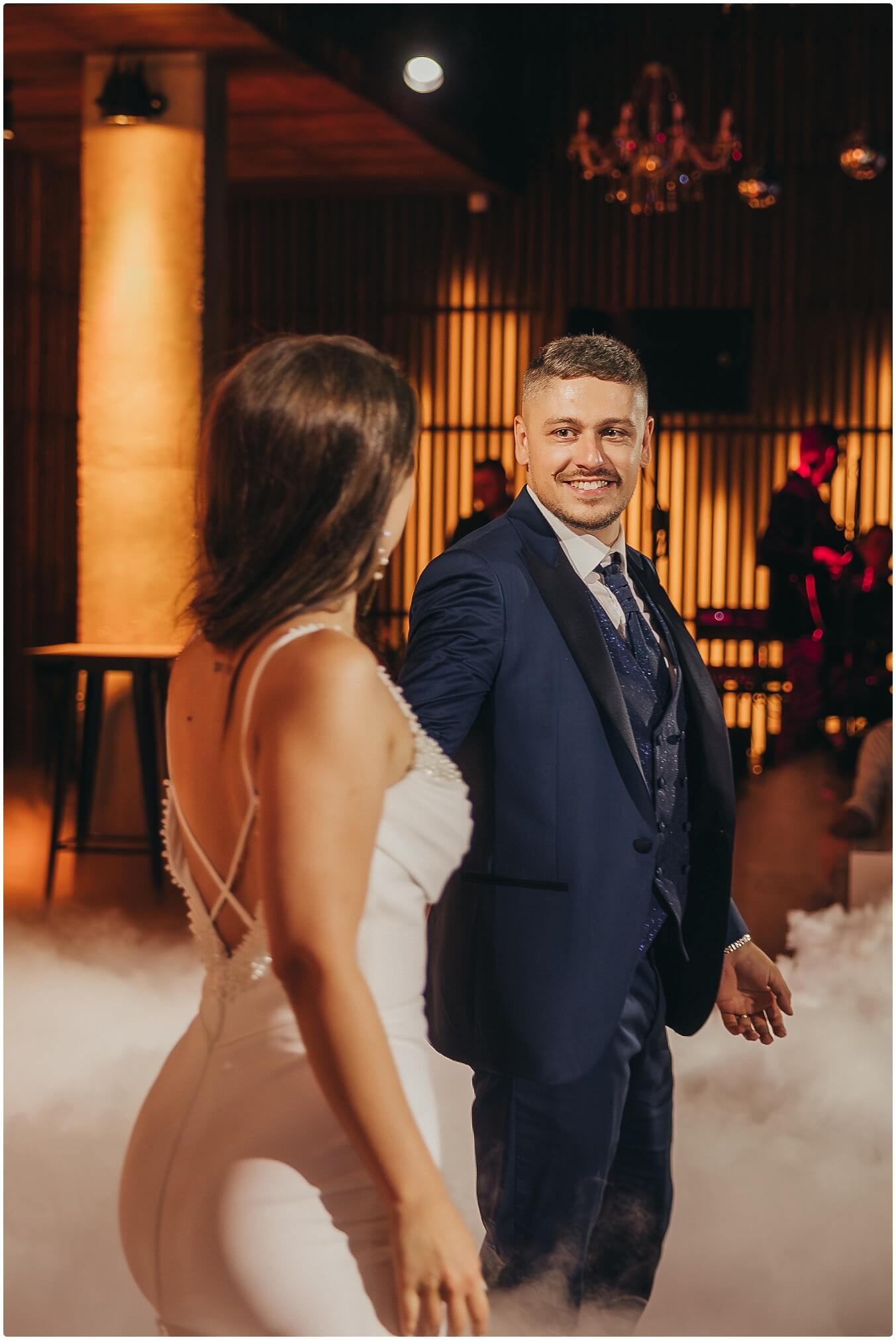 Mladenci plešu prvi ples u elegantnoj dvorani, okruženi prijateljima i svjetlima